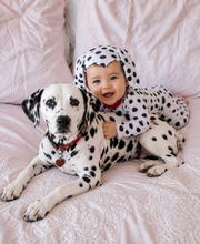 Baby in a Dalmatian costume sitting next to a Dalmatian dog on a pink blanket.