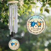 Wind chime with turtle design and engraved text hanging among green leaves.