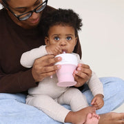 Baby drinking from a pink sippy cup held by an adult