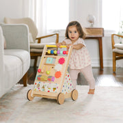 Baby girl taking first steps pushing rainbow wooden activity walker in living room