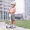 Child riding a scooter with a helmet on a sidewalk in an urban setting