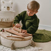 Child in a green sweater playing with wooden toys on a woven ottoman.